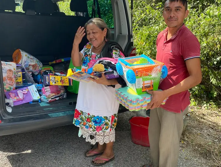 Two people stand beside an open vehicle trunk displaying colorful toys and educational materials