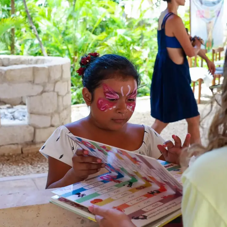 Child with face paint designs looking at a colorful worksheet while sitting outdoors in a garden setting