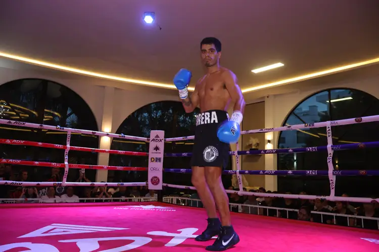 Boxer in blue gloves stands in a boxing ring with pink flooring and purple ropes in an indoor gym Boxer in blue gloves stands in a boxing ring with pink flooring and purple ropes in an indoor gym