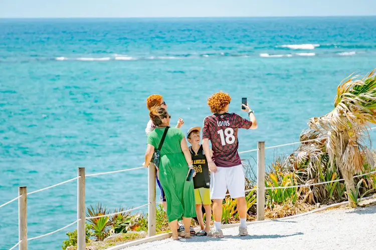 Three people stand at a coastal overlook with a railing, looking at the ocean and taking photos Three people stand at a coastal overlook with a railing, looking at the ocean and taking photos