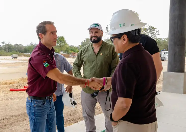Two men in maroon shirts shake hands with a man wearing a white hard hat and olive shirt at a construction site Two men in maroon shirts shake hands with a man wearing a white hard hat and olive shirt at a construction site