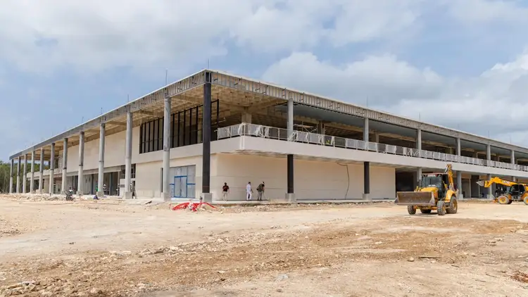Large commercial building under construction with concrete structure, steel columns and open floor levels, surrounded by sandy ground and construction equipment Large commercial building under construction with concrete structure, steel columns and open floor levels, surrounded by sandy ground and construction equipment