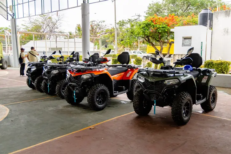 Row of all-terrain vehicles parked in an outdoor facility with staff members visible in the background Row of all-terrain vehicles parked in an outdoor facility with staff members visible in the background