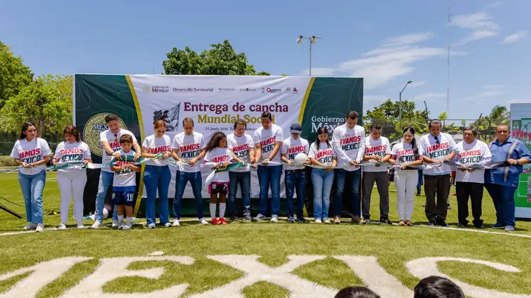 Group of people wearing matching white and red shirts stand on a soccer field in front of a large banner during an outdoor ceremony Group of people wearing matching white and red shirts stand on a soccer field in front of a large banner during an outdoor ceremony