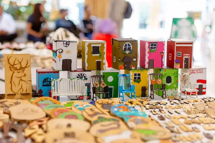 Colorful handmade wooden houses and decorative pieces displayed on a table at what appears to be a craft market or artisan event Colorful handmade wooden houses and decorative pieces displayed on a table at what appears to be a craft market or artisan event