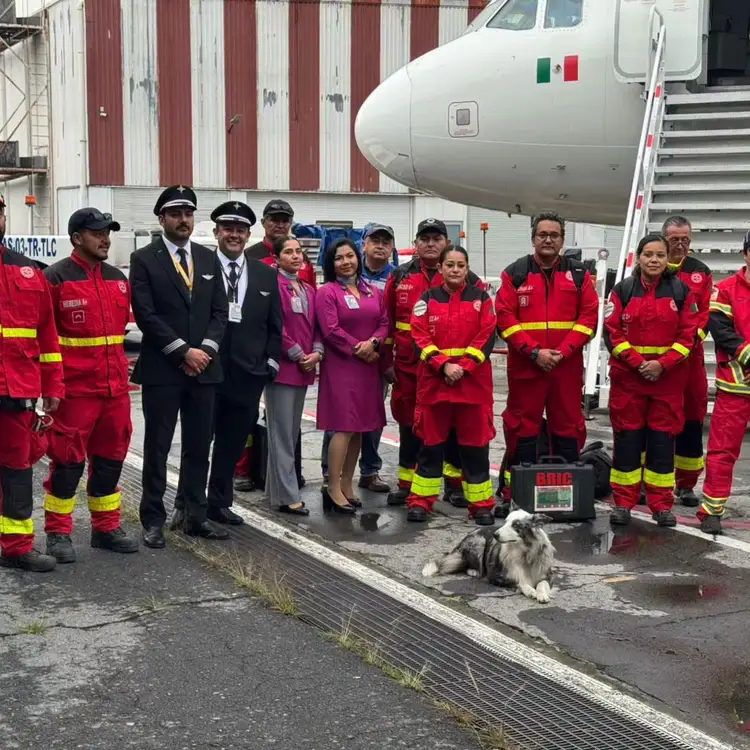 Emergency responders and officials in red uniforms stand in a line next to an aircraft bearing a Mexican flag at an airport hangar