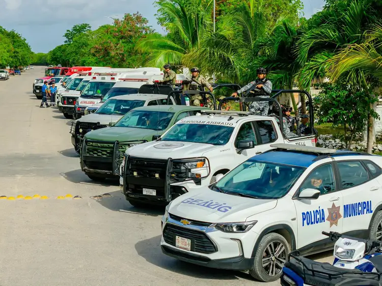 Multiple police and emergency vehicles line a paved area with tropical vegetation in the background Multiple police and emergency vehicles line a paved area with tropical vegetation in the background