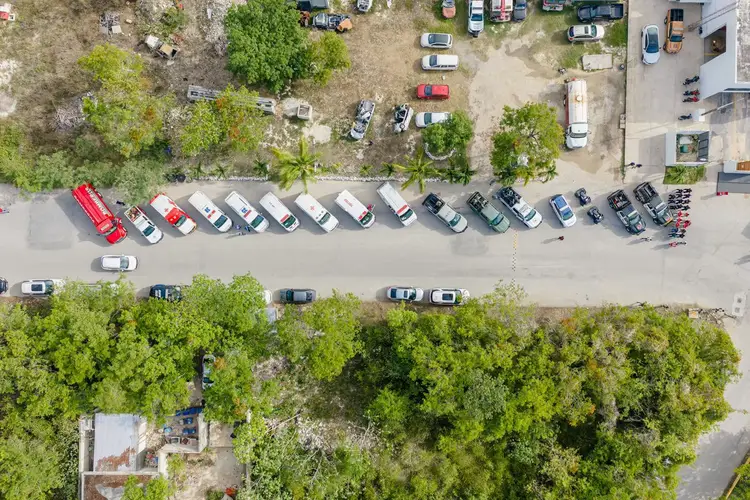 Aerial view of a parking lot with cars lined up in rows along a street bordered by trees and buildings Aerial view of a parking lot with cars lined up in rows along a street bordered by trees and buildings
