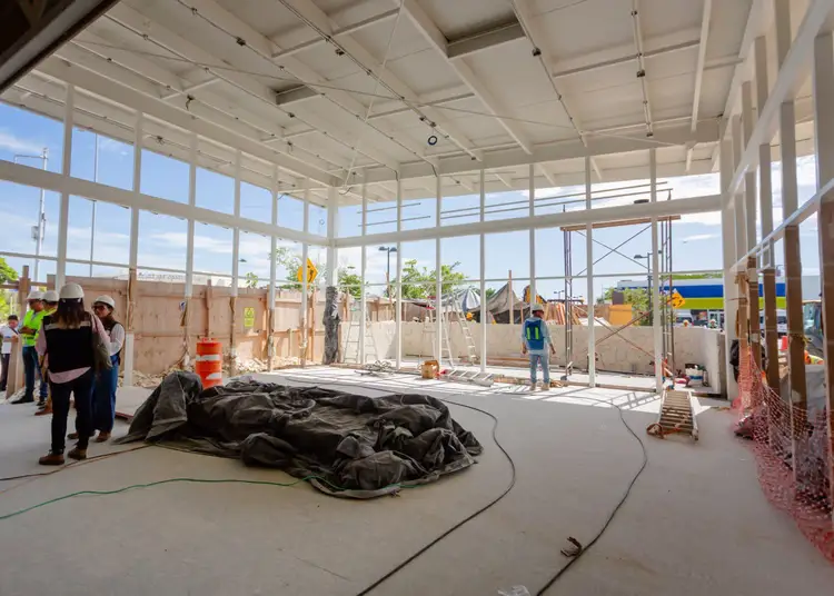 People tour a construction site inside a large glass-walled building with exposed framing and equipment visible