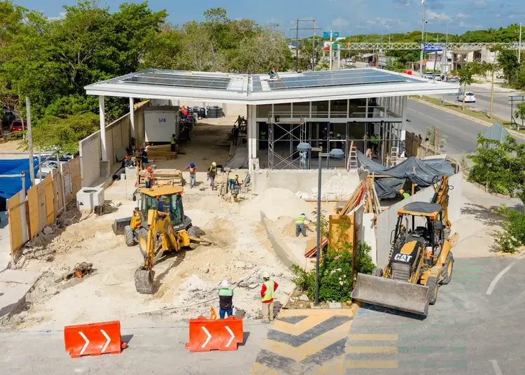 Construction workers and heavy equipment work on a new building with solar panels under construction at an active site with orange barriers and safety fencing