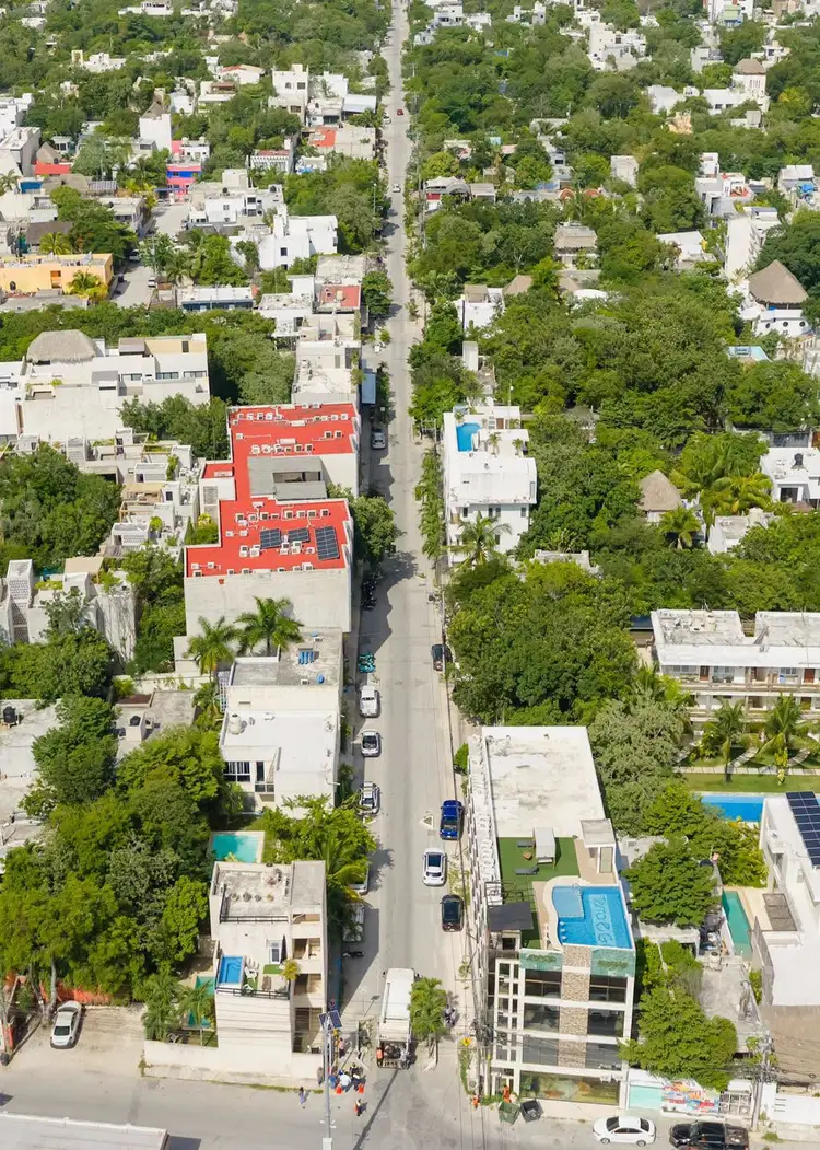 Aerial view of a residential neighborhood with a straight street running through the center, lined with white and colorful buildings surrounded by dense green t Aerial view of a residential neighborhood with a straight street running through the center, lined with white and colorful buildings surrounded by dense green t