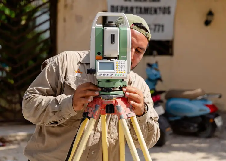 Surveyor uses a theodolite mounted on a tripod to measure and map terrain at an outdoor construction site Surveyor uses a theodolite mounted on a tripod to measure and map terrain at an outdoor construction site