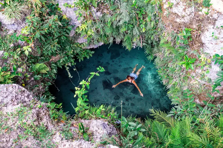 Person swimming in a natural sinkhole surrounded by rocky limestone walls and dense vegetation Person swimming in a natural sinkhole surrounded by rocky limestone walls and dense vegetation