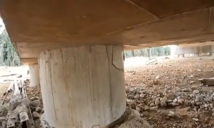 Concrete support column stands on rocky ground beneath a wooden structure, with forested landscape visible in the background