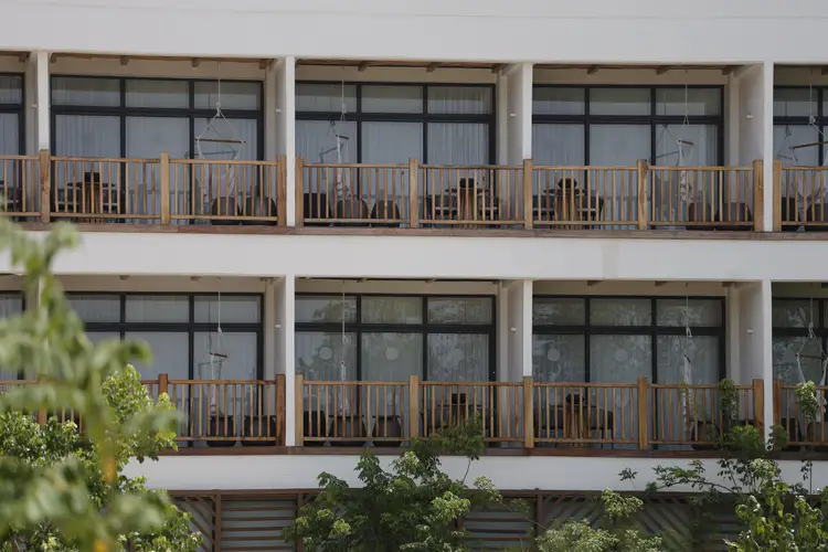 Multi-story residential or hotel building with wooden railings on balconies and large windows, with green plants visible in the foreground