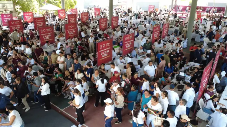 A large crowd of people fills an indoor venue with red promotional banners and signs visible throughout the space A large crowd of people fills an indoor venue with red promotional banners and signs visible throughout the space