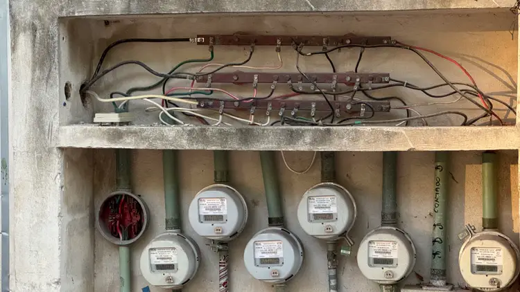 Electrical meter box with exposed wiring and multiple utility meters mounted on a concrete wall