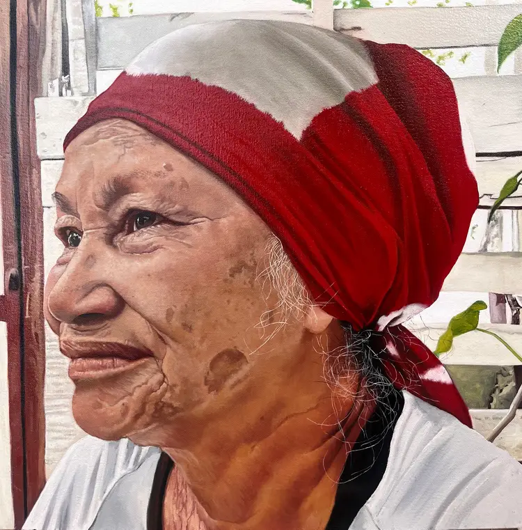 A sculptural bust of an elderly person wearing a red and white headscarf, displayed indoors near potted plants
