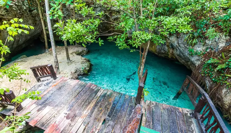 Wooden platforms overlook a turquoise cenote surrounded by limestone cliffs and dense jungle vegetation