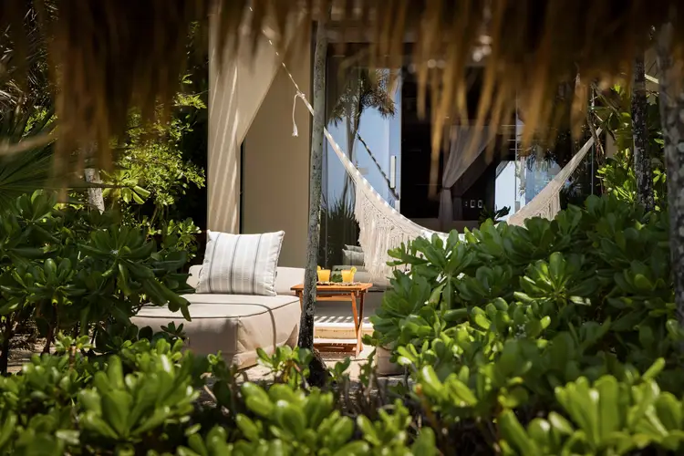 Lounge seating with cushions and hammocks nestled among lush green plants on a terrace overlooking a coastal landscape Lounge seating with cushions and hammocks nestled among lush green plants on a terrace overlooking a coastal landscape