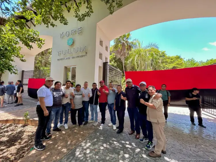 Group of workers gathered in front of a building with red wall and "Kore Tulum" signage, appearing to assemble for a protest or meeting Group of workers gathered in front of a building with red wall and "Kore Tulum" signage, appearing to assemble for a protest or meeting