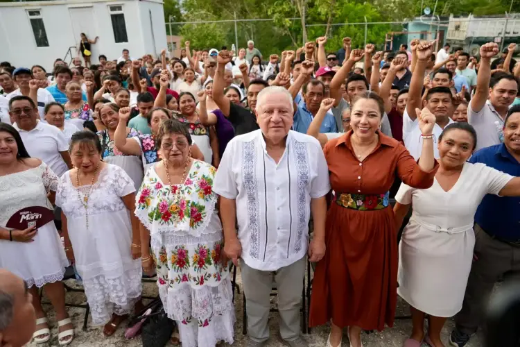 Large crowd of people gathered outdoors with raised fists, several wearing traditional embroidered clothing in the foreground