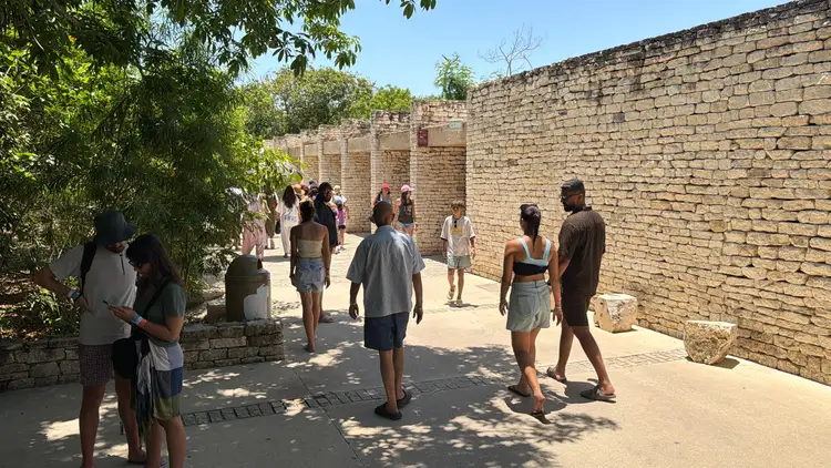 Visitors walk through a stone-walled pathway at an archaeological site on a sunny day Visitors walk through a stone-walled pathway at an archaeological site on a sunny day