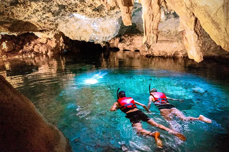 Two snorkelers float in clear turquoise water inside a cave surrounded by rocky limestone formations Two snorkelers float in clear turquoise water inside a cave surrounded by rocky limestone formations
