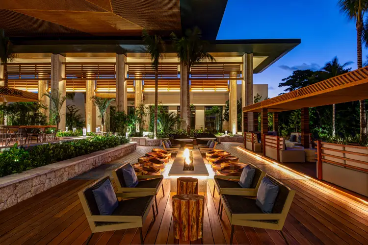 Patio de resort moderno en Tulum luce fogata central rodeada de camastros, con edificios iluminados y vegetación tropical de fondo Patio de resort moderno en Tulum luce fogata central rodeada de camastros, con edificios iluminados y vegetación tropical de fondo