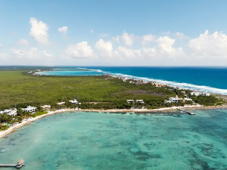 Aerial view of a coastal resort area with turquoise shallow waters, sandy beaches, vegetation, and lagoon alongside deeper blue ocean Aerial view of a coastal resort area with turquoise shallow waters, sandy beaches, vegetation, and lagoon alongside deeper blue ocean