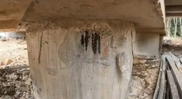 Concrete support pillar showing deterioration and erosion damage beneath an elevated structure in a construction area