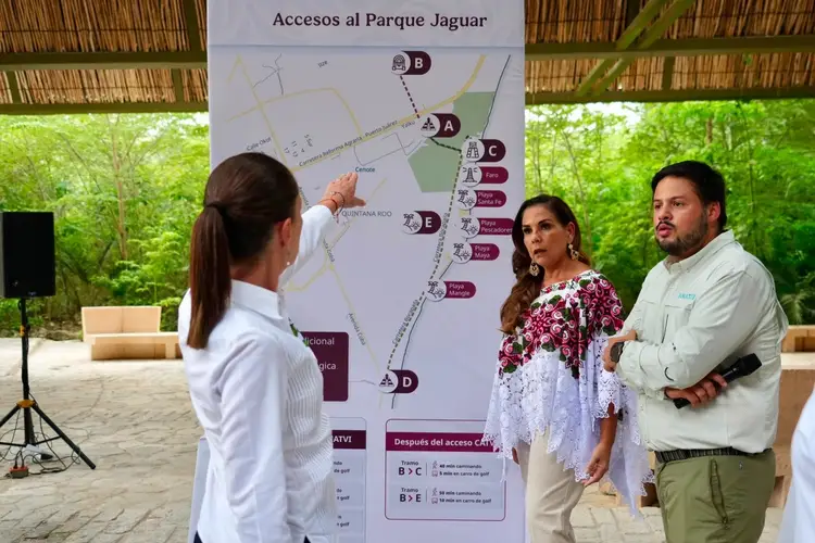 Two people discuss a map labeled "Accesos al Parque Jaguar" while standing in an open-air venue with another person listening