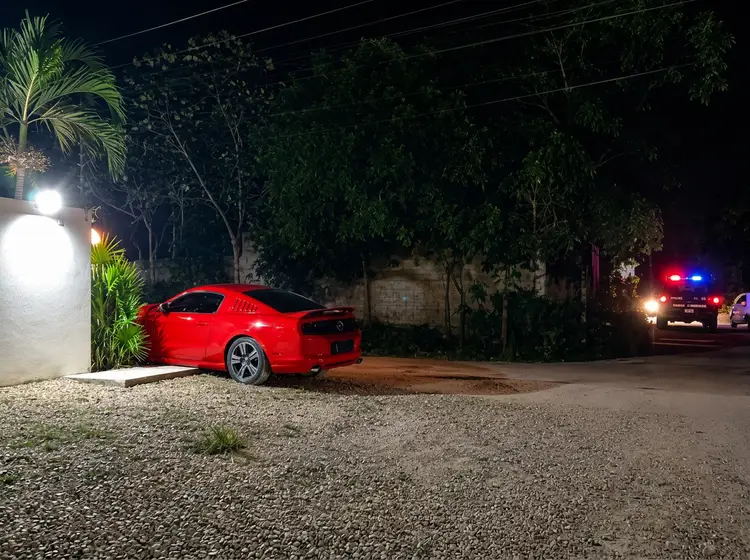 Red sports car parked at night in a residential area with emergency vehicles visible in the distance Red sports car parked at night in a residential area with emergency vehicles visible in the distance
