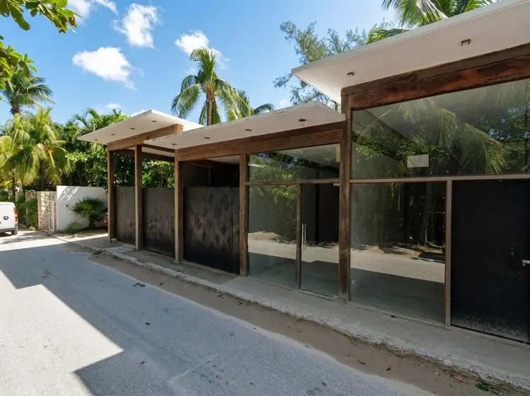 Modern commercial structure with dark glass panels and wooden beams sits empty along a paved street lined with palm trees