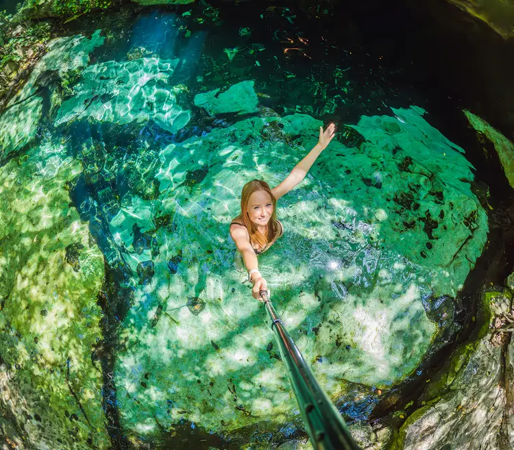 Woman swimming in a cenote with turquoise water surrounded by limestone cave walls and moss-covered rock formations Woman swimming in a cenote with turquoise water surrounded by limestone cave walls and moss-covered rock formations
