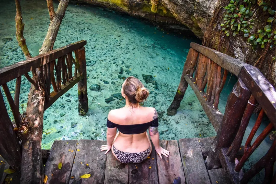 Person sitting on a wooden platform above clear turquoise water surrounded by rock formations and wooden railings