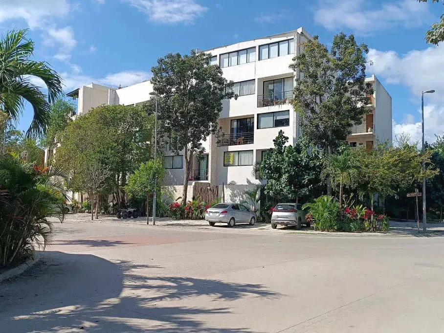 Rising Real Estate Fraud Alarms Tulum Investors and Residents Modern white apartment building with multiple stories surrounded by tropical vegetation and parked cars on a paved street