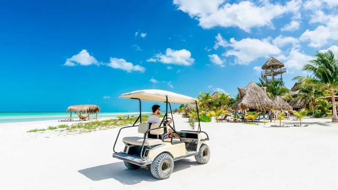 Tulum Approves 400 Golf Carts Amid Traffic Innovation Push Golf cart parked on white sand beach with thatched-roof structures and palm trees visible along the shoreline