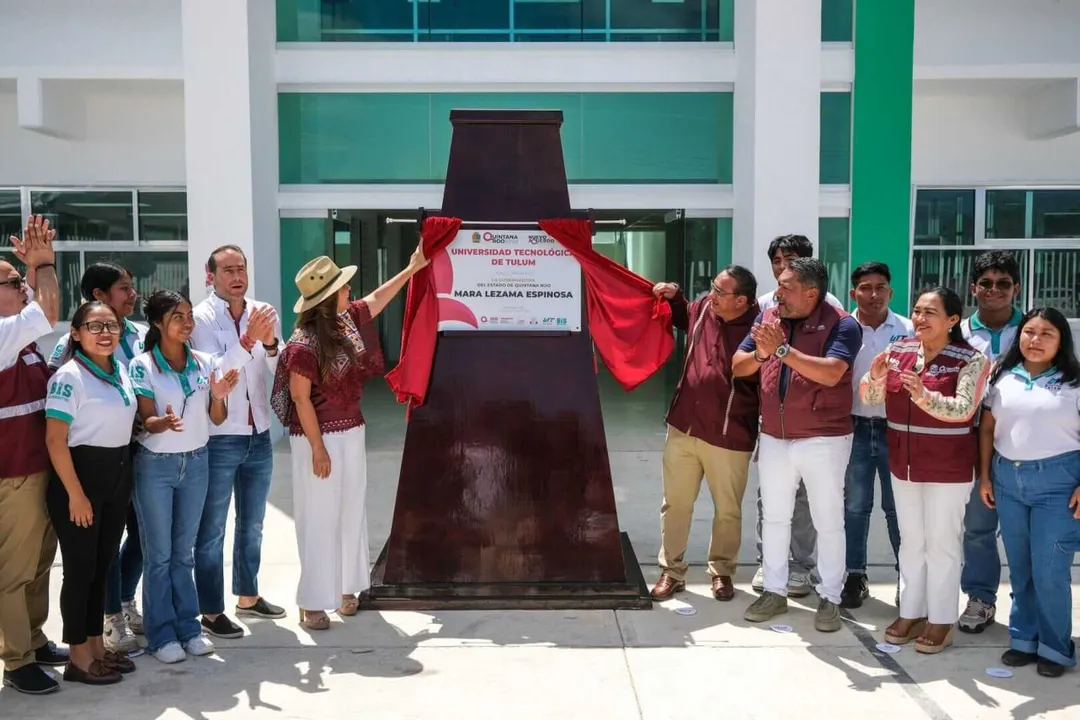 Group of people unveiling a large bronze monument or sculpture in front of a modern building with green and white facade