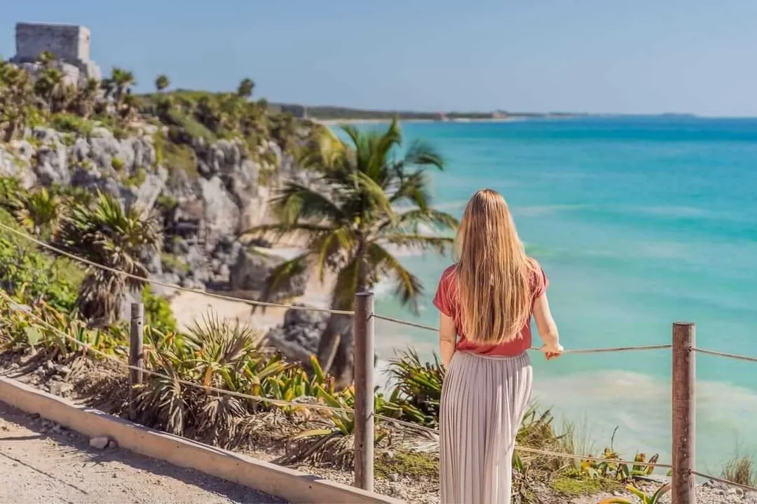 Mexico’s Coasts: Secure Sanctuaries for Women Travelers Woman with long hair standing on a clifftop overlooking turquoise water and rocky coastline with palm trees and a distant stone structure