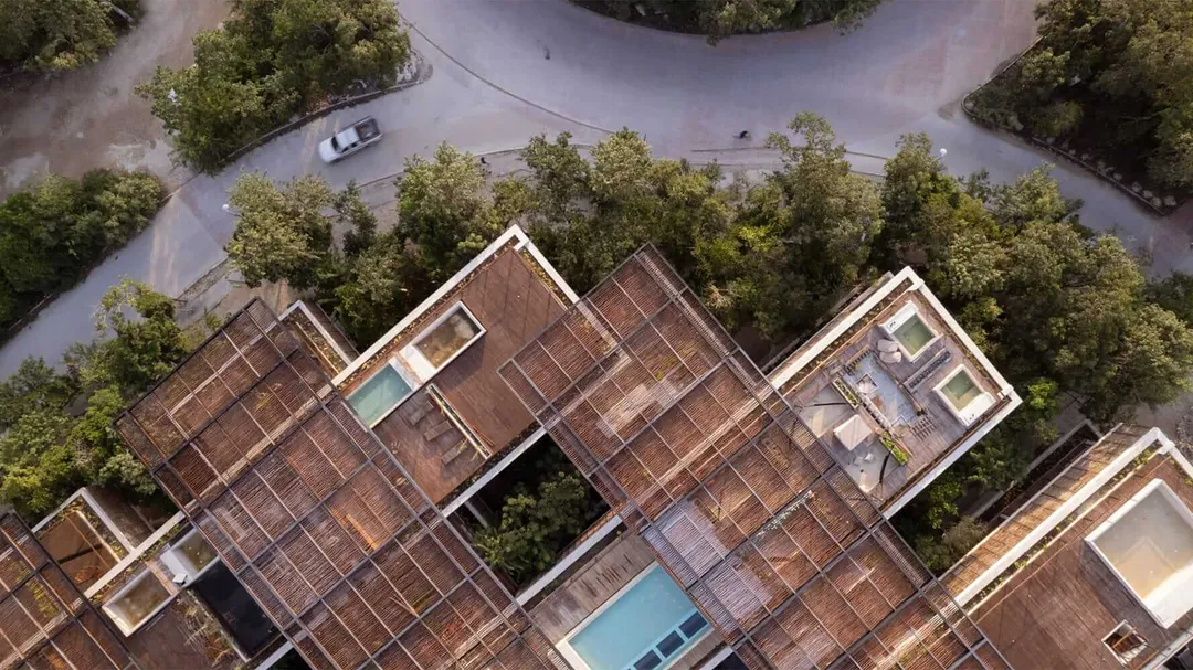 Aerial view of residential buildings with terracotta tile roofs surrounded by trees and a winding street with a parked vehicle
