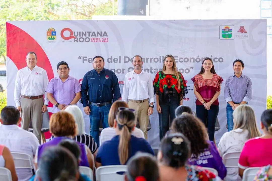 Seven officials stand on stage before an audience at an event with a Quintana Roo banner behind them