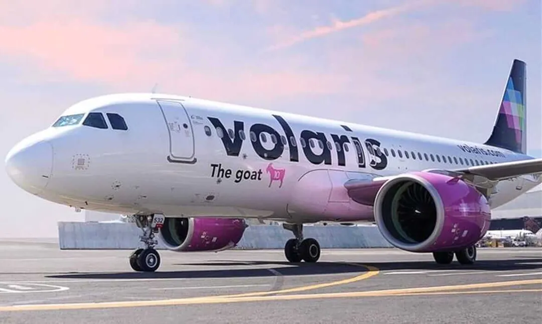 Commercial aircraft with purple and white livery parked on an airport tarmac under a light sky