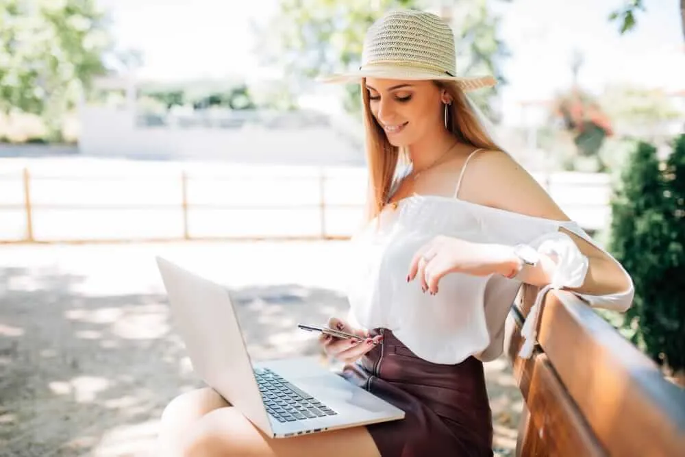 Real Estate Platform Gains 500 Members in Two Weeks Woman in a straw hat and white top works on a laptop while holding a pen on a sunny outdoor patio