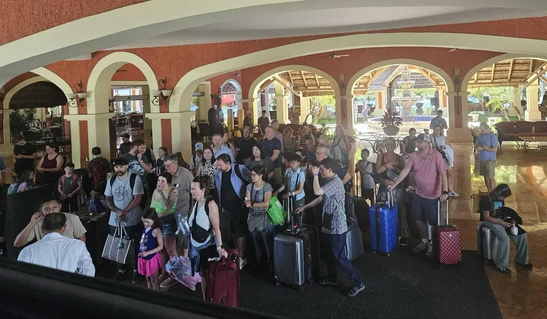 WestJet Faces Flight Delays Amid Tulum Travel Disruptions Large crowd of travelers with luggage gathered in an arched terminal building with terra cotta walls and cream-colored columns