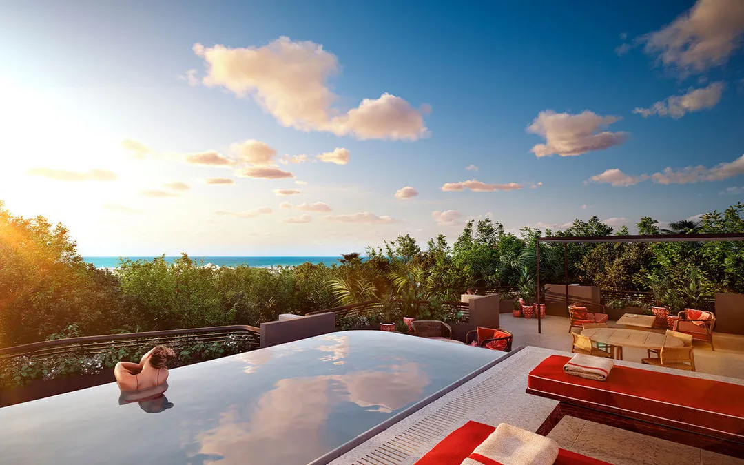 Faena Tulum and the Rise of Symbolic Real Estate A person sits in an infinity pool overlooking tropical vegetation and ocean waters under a partly cloudy sky at sunset