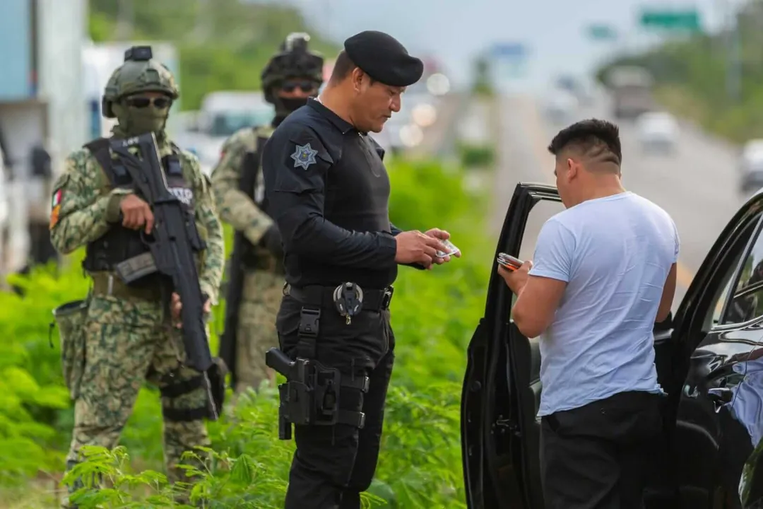 Tulum Hotels Near 92% Occupancy During Holiday Season Police officer speaks with a man beside a vehicle while armed military personnel stand nearby on a roadside
