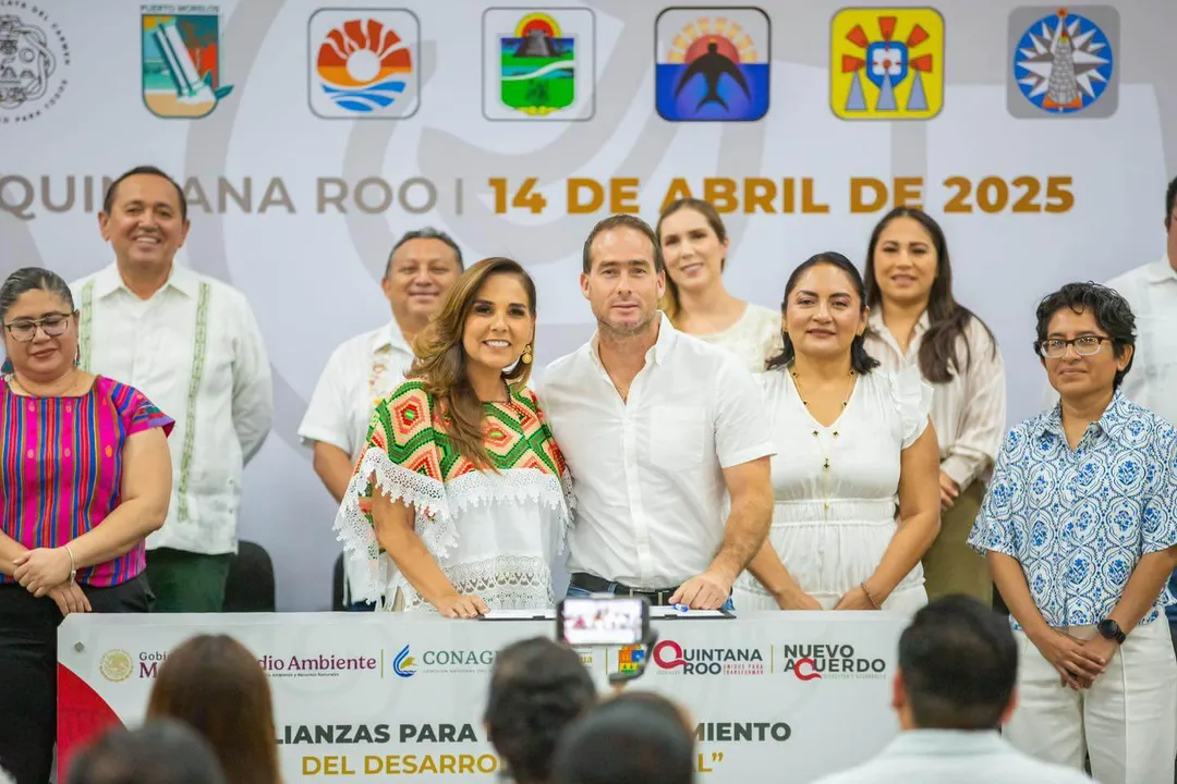 Group of officials and community members stand together at a podium during a public event in Quintana Roo, with municipal emblems displayed above them