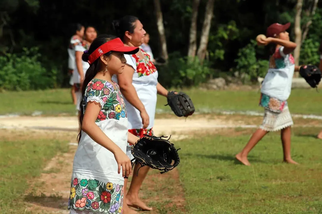 Young softball players in fielding positions on a grass field surrounded by trees during a game