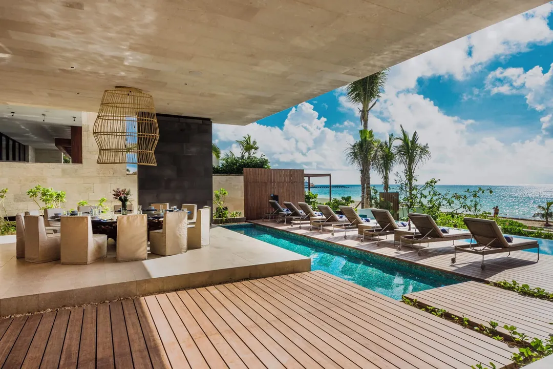 Modern beachfront resort with infinity pool, lounge chairs, palm trees, and ocean view overlooking a tropical coastline